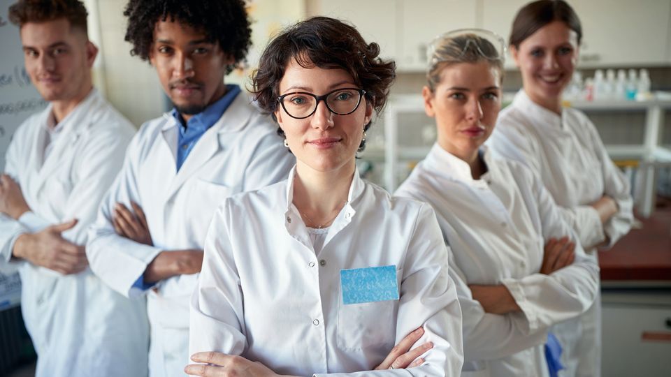 A group of life scientists in lab coats facing the camera, arms crossed with challenging looks on their faces.
