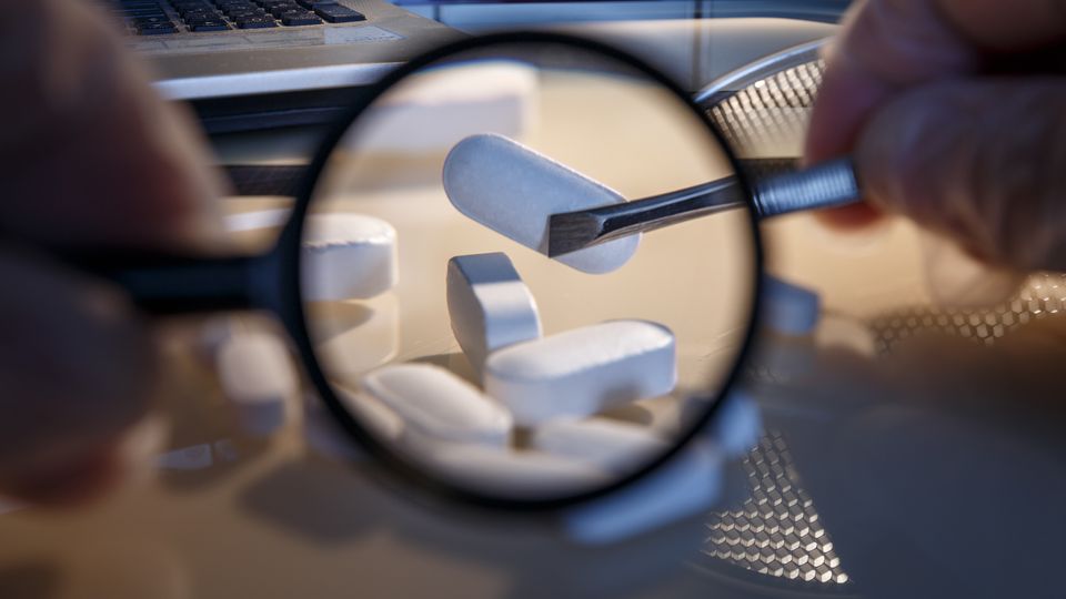 Close-up of white metformin tablets examined with magnifying glass and tweezers.