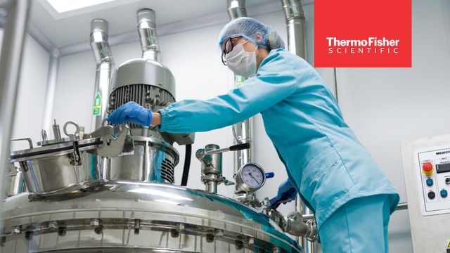 Researcher adjusting controls on a large bioreactor for therapeutic protein production 