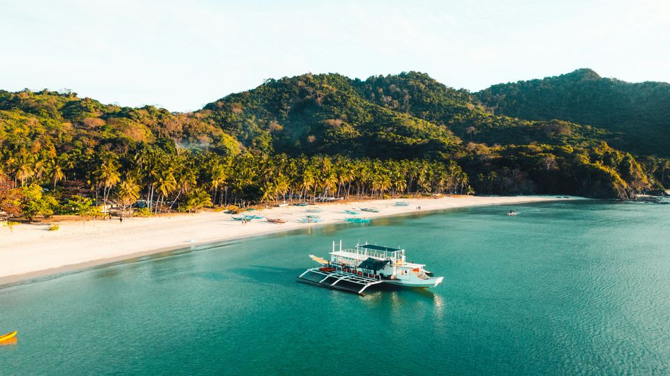 A boat resting in the shallows near a tropical beach. Hills of jungle beyond.