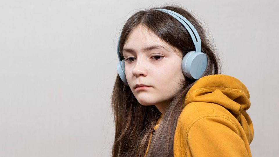 Young girl with headphones wearing a yellow hoodie, representing autism and sensory sensitivity.