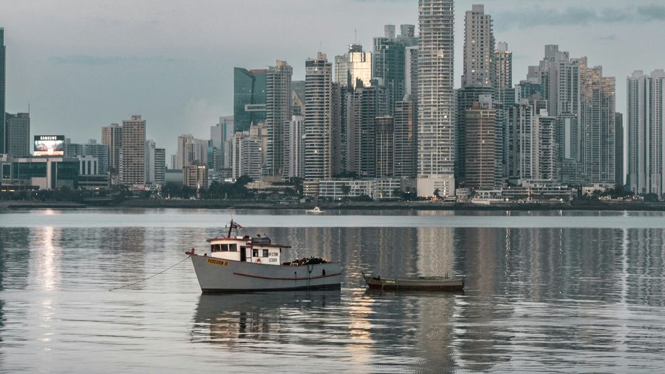 A small boat sits on the water in front of the Panama City skyline.