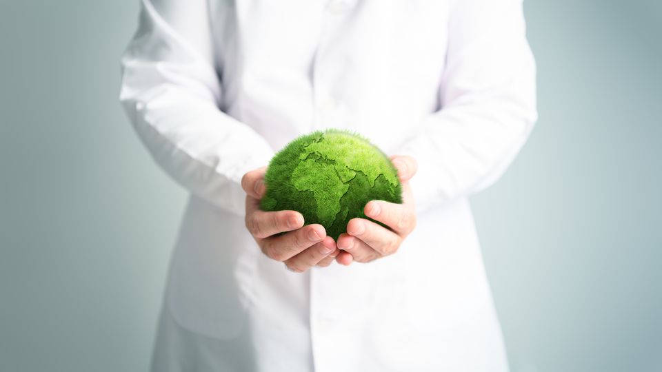A scientist holding a digitally-superimposed globe in their hands, which is designed to look like it is made of grass or moss.