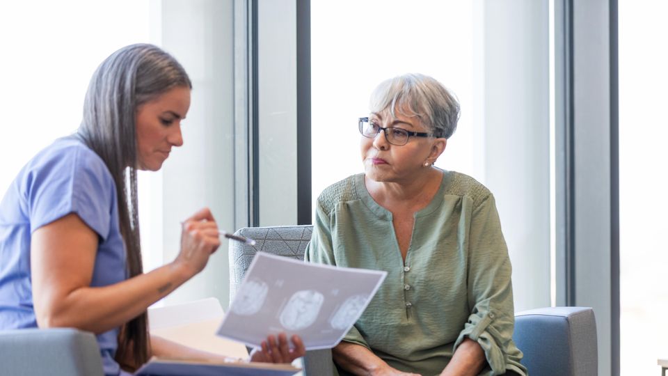 Female doctor discussing brain scan results with senior woman during Alzheimer's consultation.