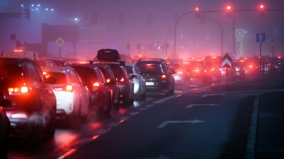 A traffic jam, shown from behind, red brake lights flash in the gloom.