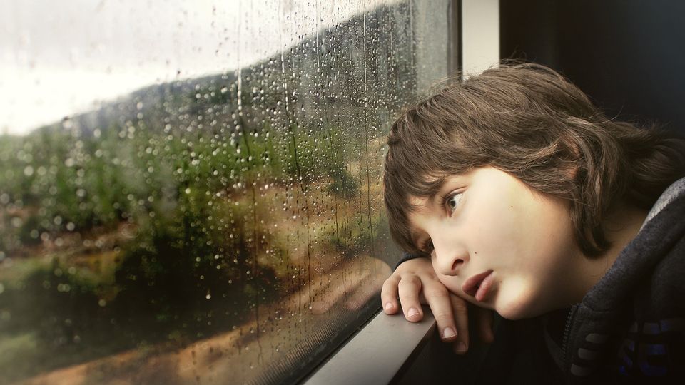Sad child leaning against a rainy window, symbolizing early life stress and emotional struggle.
