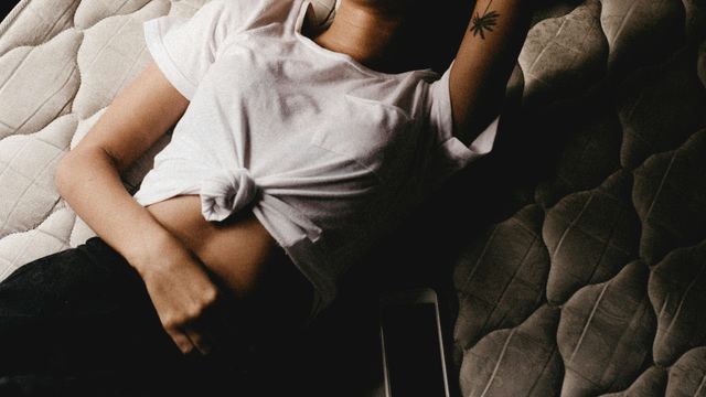 A person lying on a mattress, their arm across their stomach. 