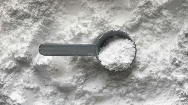 Scoop of white creatine powder supplement on a textured surface. 