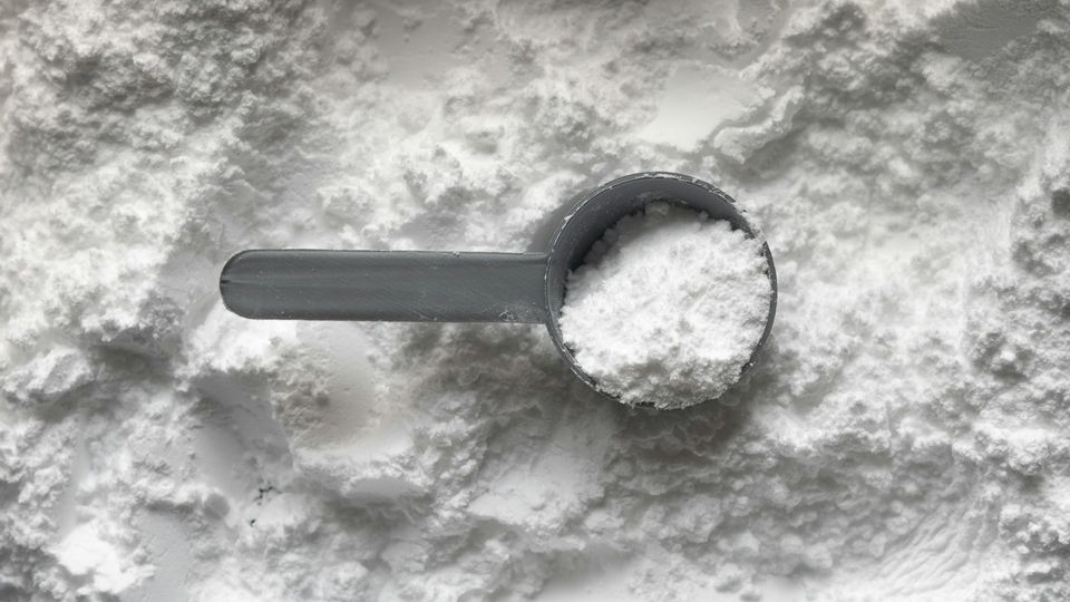 Scoop of white creatine powder supplement on a textured surface.
