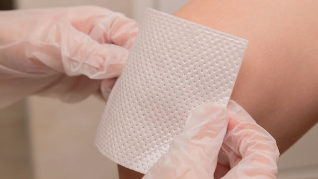 Gloved hands apply a square of gauze to a knee.