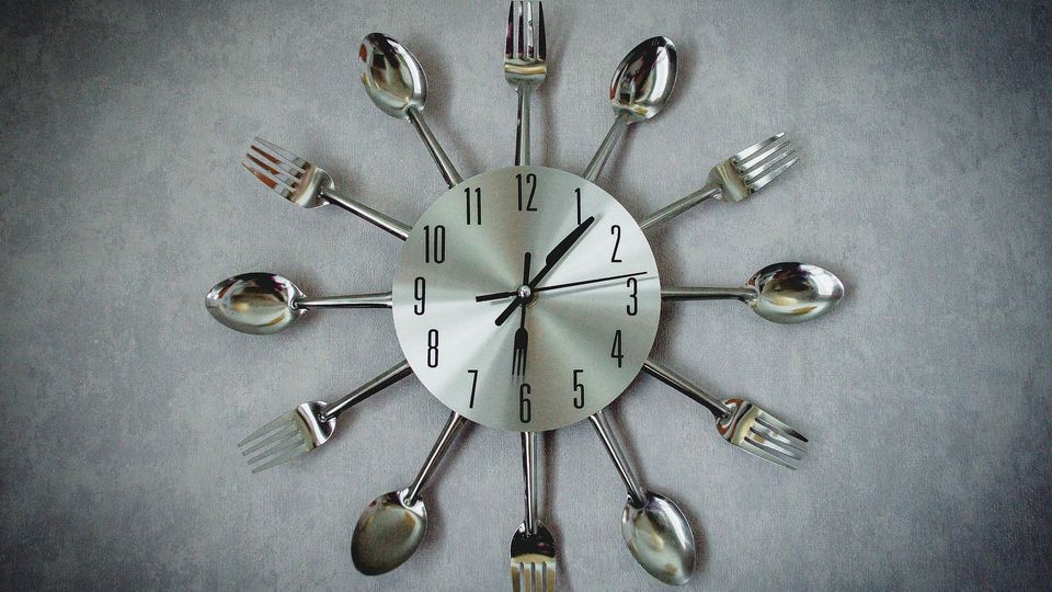 A silver clock with knives, forks and spoons around the outside.