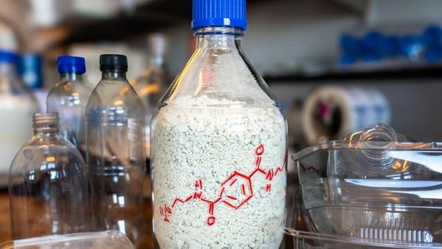 A tall glass bottle filled with the BAETA material made by upcycling PET plastic waste.