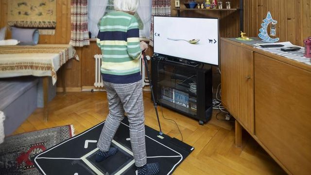 Elderly woman using a motion-sensing game system for game-based physical training at home.