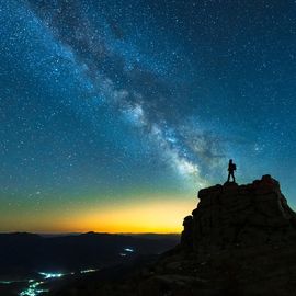 Starry night sky with a lone explorer on a peak, representing imagination and night science. 