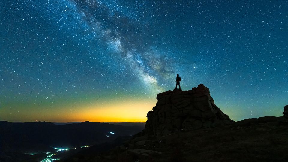 Starry night sky with a lone explorer on a peak, representing imagination and night science.