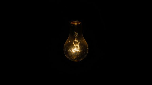 Glowing light bulb in darkness symbolizing illumination and ideas. 
