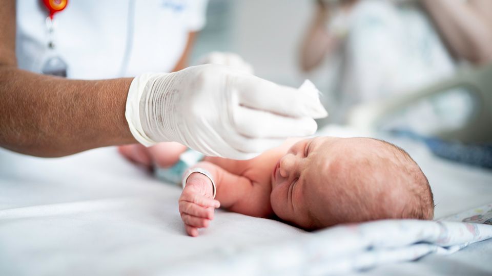 A newborn baby in hospital with a nurse leaning over administering treatment in preparation for LNP-mediated gene therapy.