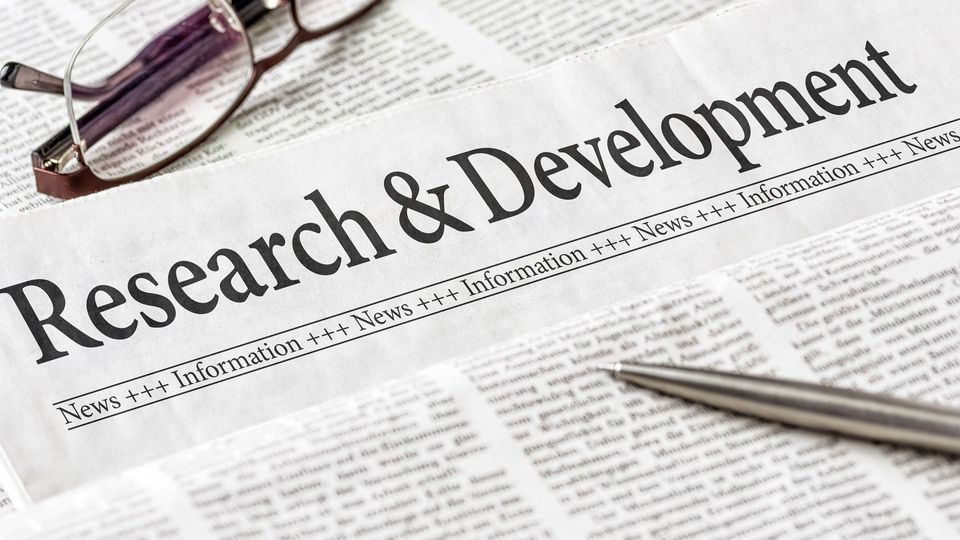 Newspaper titled "Research & Development", with a pen lying on top.