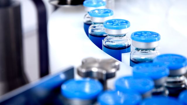 Blue-capped vaccine vials on a production line in a pharmaceutical facility. 