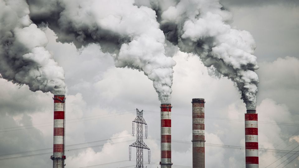 Gray smoke billowing from a number of red and white smokestacks, against a gray cloudy sky.