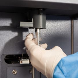 Gloved hand operating a flow cytometry machine, inserting a sample tube for cell analysis. 