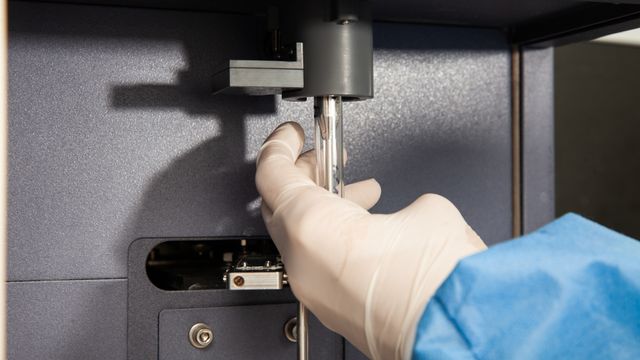 Gloved hand operating a flow cytometry machine, inserting a sample tube for cell analysis. 