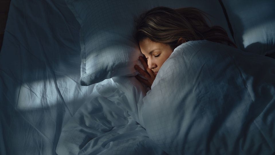 Woman sleeping peacefully under a blanket in a dimly lit bedroom, representing restful sleep during cooler nights.