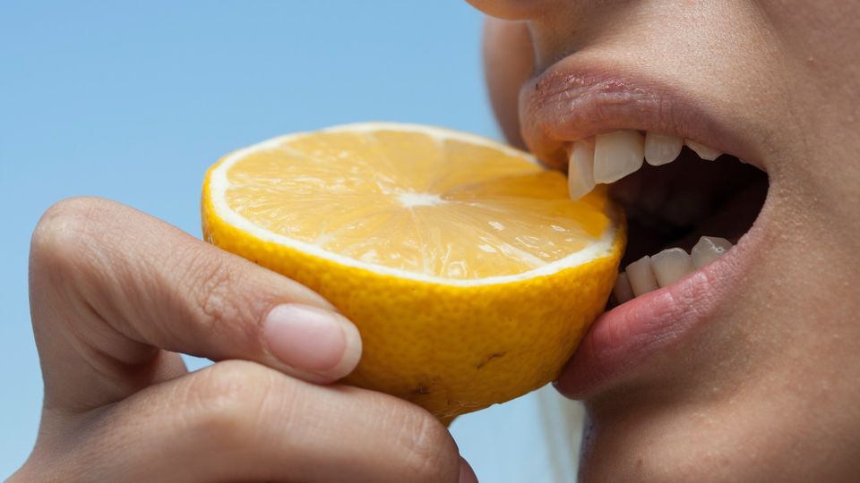Close-up of a person tasting a fresh lemon slice, highlighting the sense of taste and sour flavor perception.
