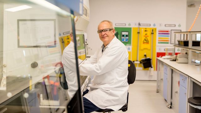 Scientist in a laboratory wearing a white coat and safety glasses, conducting research on antibodies inside a biosafety cabinet. 