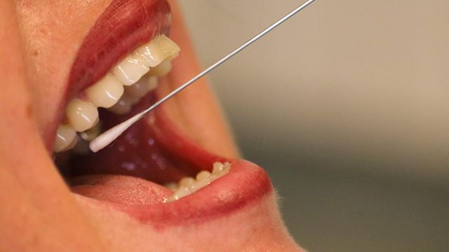 A woman with red lipstick using a cheek swab. 