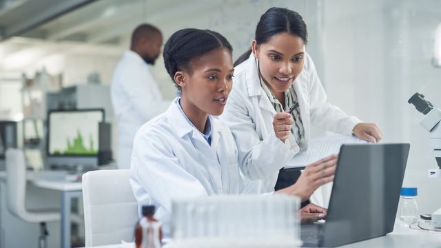 Two female scientists reviewing data on a laptop in a modern research laboratory. 
