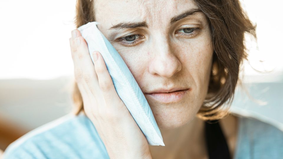 A women holding a wet cloth to her face suffering from hot sweats, a common symptom of menopause.