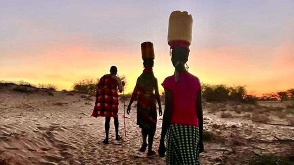Three members of Kenya's Turkana community, walking through the desert with water jugs balanced on their heads. 