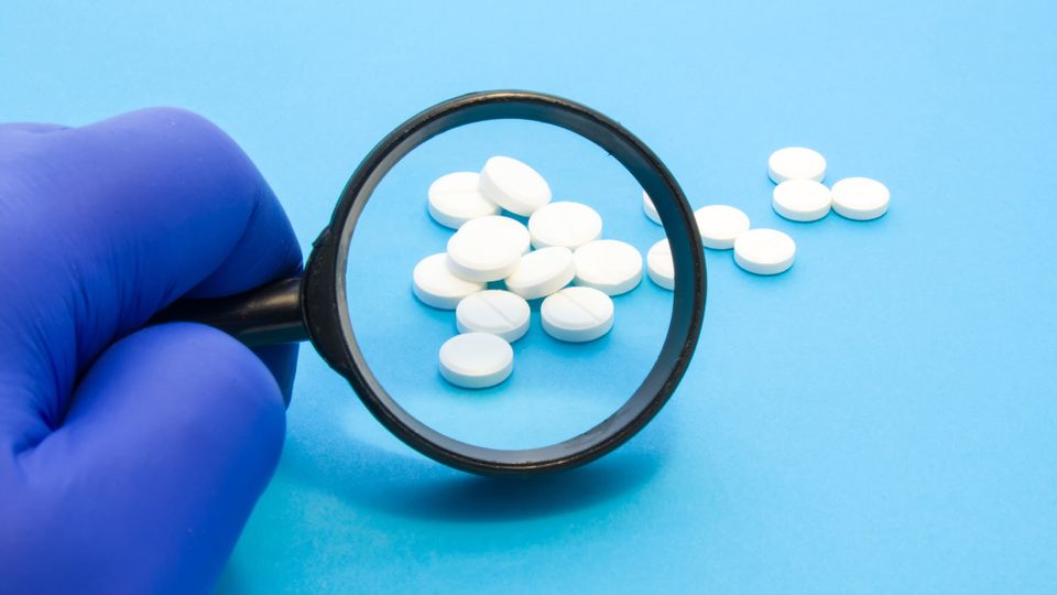 Gloved hand examining white tablets with magnifying glass, representing oral semaglutide research.