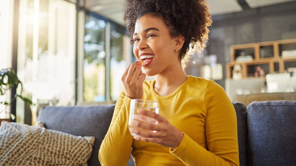 A woman in a yellow top taking a vitamin supplement with a glass of water.