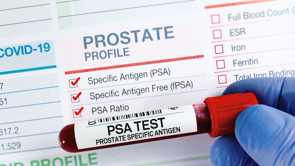 Full blood tube being held by blue gloved hand in front of prostate cancer screening sheet.