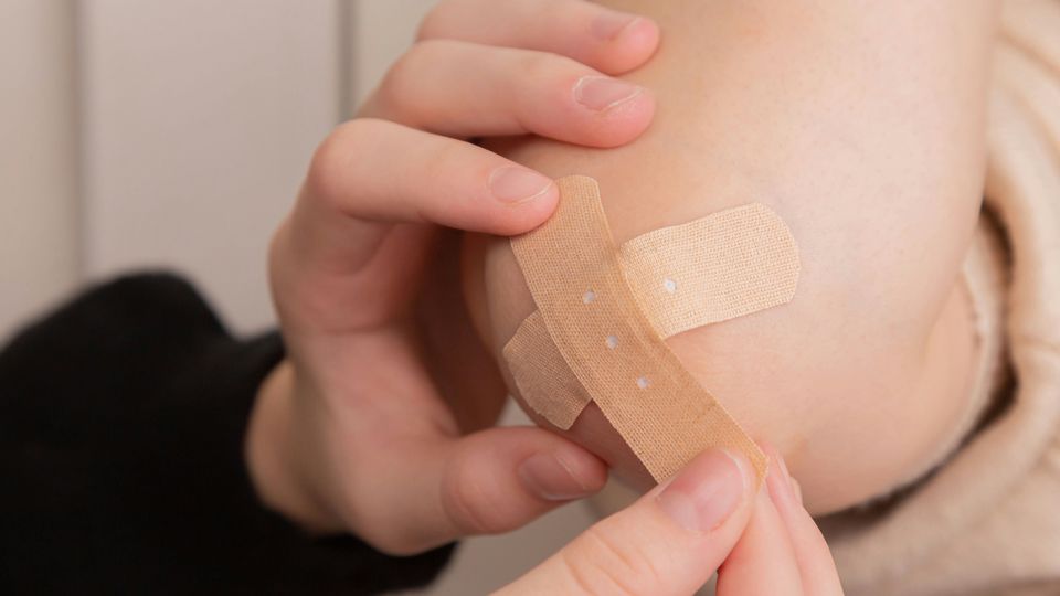 A woman putting a Band-Aid on a child's elbow.