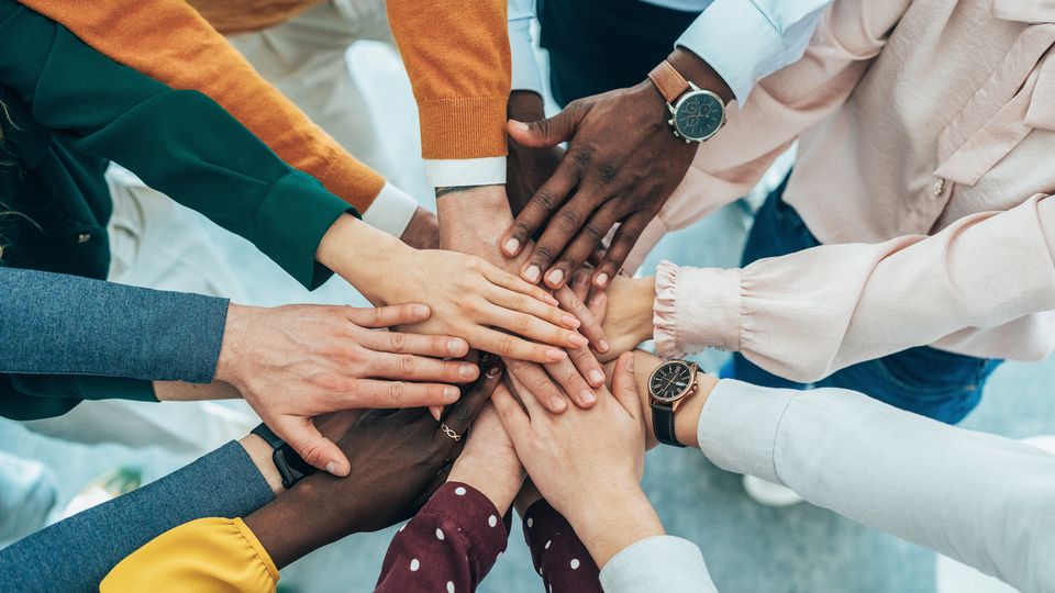 People standing around in a circle holing their hands out in the middle, representing and collaboration team work.