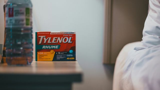 A packet of Tylenol stands on a bedside table near a bottle of water. 