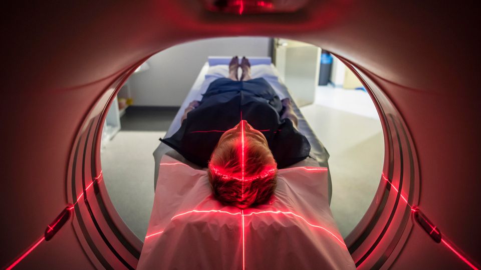 Patient undergoing brain imaging scan with red laser alignment in MRI machine.