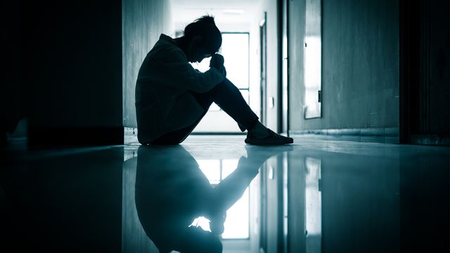 A woman suffering from depression sitting alone in a dark corridor. 