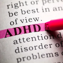 The word ADHD highlighted in pink on a printed page with a marker.