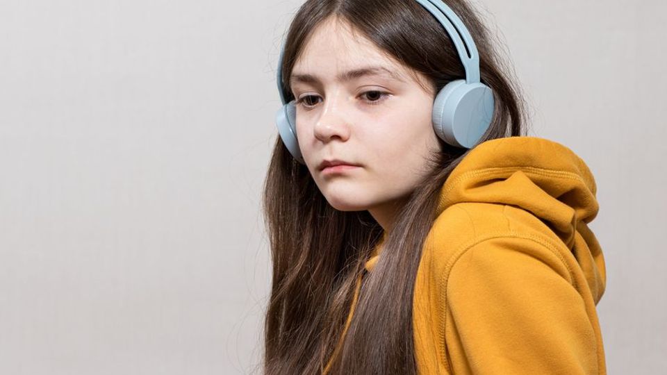 Young girl in a yellow hoodie wearing headphones, appearing withdrawn, often associated with autism.