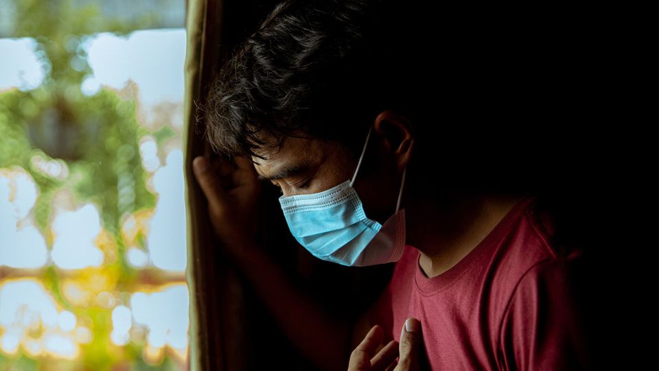 A man suffering from COVID-19 in a face mask holding his chest.