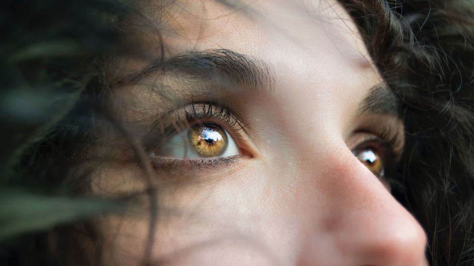 A person with curly hair and hazel eyes looks skyward.