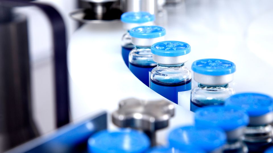A production line of vaccine vials containing a blue liquid.