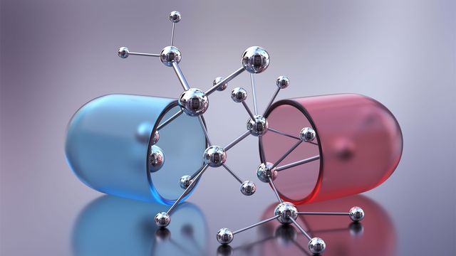 red and blue drug capsule split in half with silver beaded molecule spilling out. 