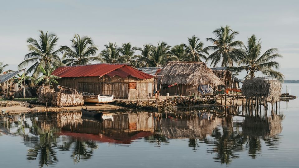 Picturesque tropical village, nestled along the water's edge, surrounded by swaying palm trees and traditional thatched-roof homes.
