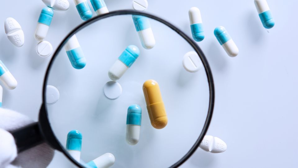 A scientist looking through a magnifying glass at a variety of different pills.