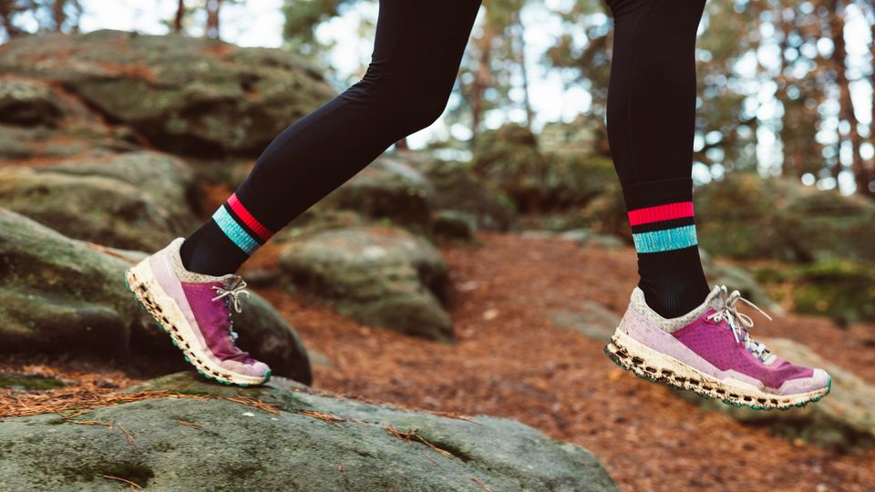 A woman in running shoes, running though a rocky trail covered in brown autumn leaves.